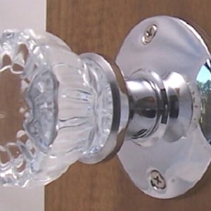May include: A chrome door knob with a clear glass crystal knob. The knob has a round, flat backplate with two screws.