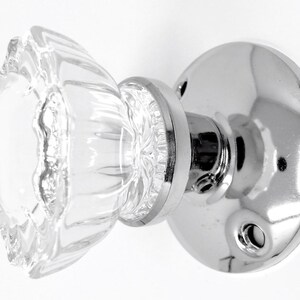 May include: A clear glass door knob with a fluted design and a shiny chrome base. The knob is round and has a textured surface. The chrome base is circular with screw holes.