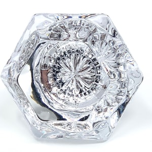 May include: A clear glass hexagonal knob with a decorative, starburst-like pattern on the top.
