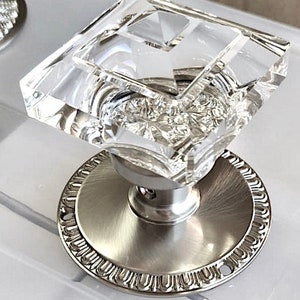 May include: A crystal door knob with a faceted design and a silver base. The base has a decorative, ornate edge.