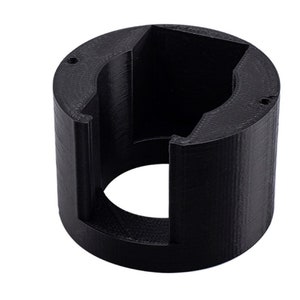 May include: A black, 3D-printed cylindrical object with a square-shaped interior and two small holes. The object has a textured surface and a circular opening on one side. The design suggests a tool or component for a larger device.