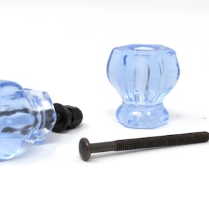 May include: Light blue glass cabinet knobs with dark bronze hardware. The set includes two knobs, a bolt, and two black nuts. The knobs have a faceted design and are suitable for furniture or cabinet upgrades.