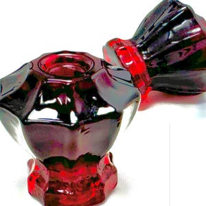 May include: Two faceted, deep red glass knobs with a multi-sided, star-like geometric shape. Each knob features a smooth, reflective surface and a central circular indentation on the top, showcasing a translucent, vibrant crimson color throughout.