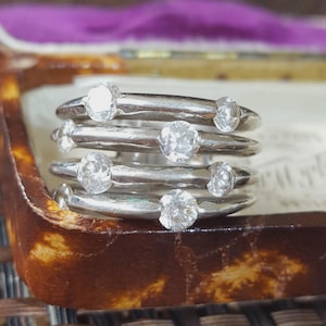 Op de afbeelding: Een zilveren ring met meerdere banden, bestaande uit vier afzonderlijke ringen die met elkaar verbonden zijn. Elke band is bezet met kleine, ronde, heldere en gefacetteerde stenen die het licht vangen. Het metaal heeft een gladde afwerking.