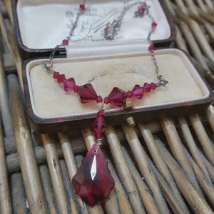 Peut inclure: Un collier vintage avec une chaîne argentée et un pendentif. Le collier présente des perles de cristal rouge foncé à facettes et un grand pendentif en forme de goutte. Le collier est présenté dans un écrin à bijoux marron doublé de velours.