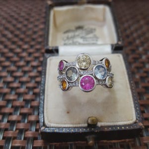 Peut inclure: Une bague en argent ornée de multiples pierres précieuses colorées, dont du rose, du jaune et du bleu, disposées dans un motif de bulles. La bague est présentée dans un écrin à bijoux vintage.