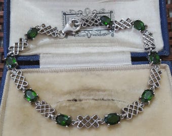 May include: Silver bracelet featuring oval green gemstones and intricate openwork links. The bracelet is presented in a blue jewellery box with a cream interior. The clasp is visible, and the piece has a vintage aesthetic.