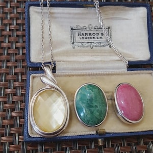 May include: A silver necklace with a large, oval, yellow gemstone pendant and two matching oval gemstones, one green and one pink, in a blue jewelry box. The box is marked "HARROD'S LONDON.S.W."