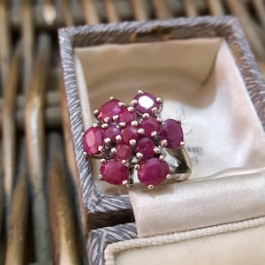 Könnte beinhalten: Ein silberner Ring mit einem Cluster aus rubinroten Edelsteinen, die in Form einer Blume gefasst sind.