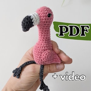 May include: A small pink flamingo crochet toy with a white and black beak, dark gray legs, and a black eye. The image includes the text PDF and + video, indicating this is a digital pattern for creating the flamingo toy through crochet.