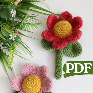 Puede incluir: Dos juguetes de flores de crochet, uno rojo con hojas verdes y otro rosa con hojas verdes. Ambas flores tienen centros amarillos. El texto "PDF" está escrito en verde sobre un fondo blanco.