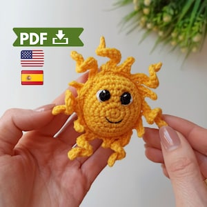 May include: A crocheted yellow sun with a smiling face and black eyes. The sun has a crocheted yellow halo with a 3D effect.