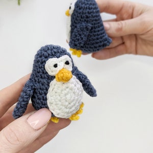 Pode incluir: Dois brinquedos de pinguim de croch&ecirc;. Um pinguim &eacute; azul com a barriga branca e o bico e as patas amarelas. O outro pinguim &eacute; azul com o bico e as patas amarelas.