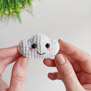 May include: A white crocheted cloud with a smiling face, black eyes, and pink cheeks.