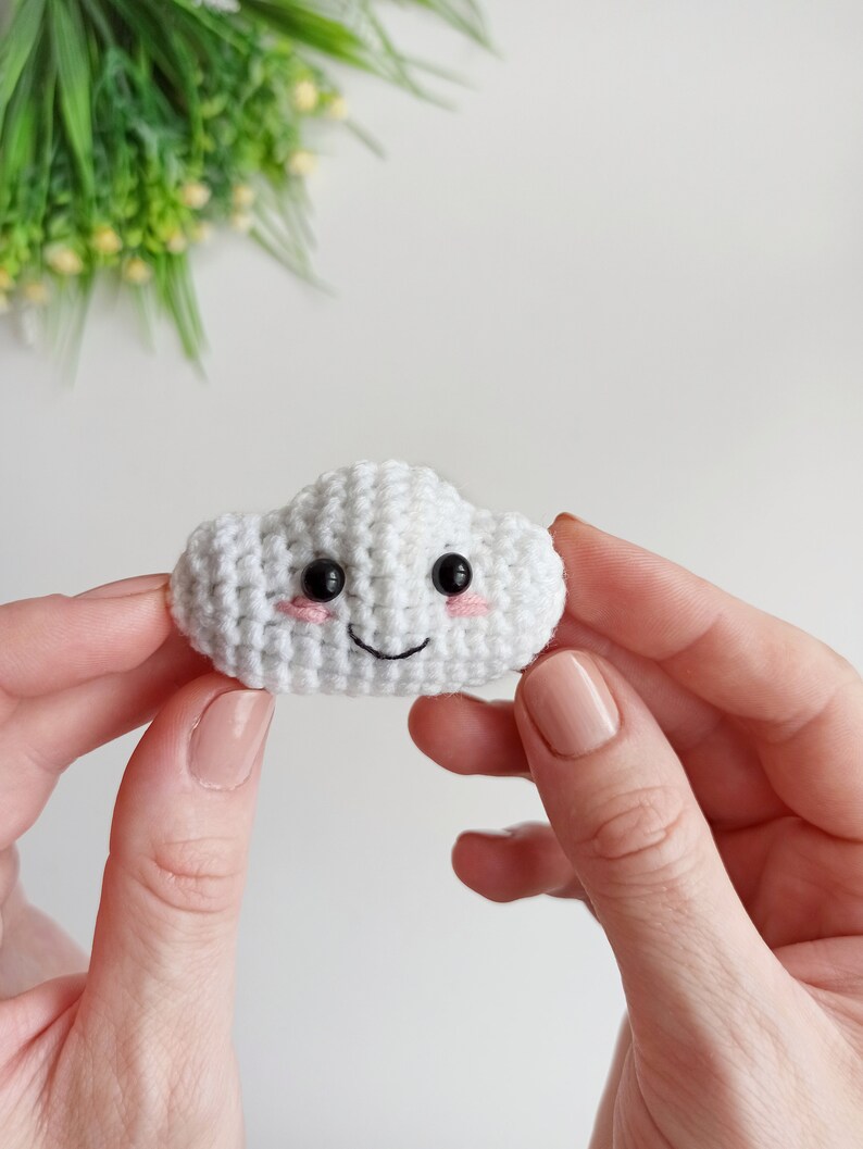 May include: A white crocheted cloud with a smiling face, black eyes, and pink cheeks.