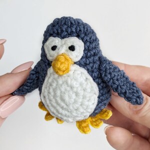 Pode incluir: Um pequeno brinquedo de pinguim de croch&ecirc; com corpo azul, barriga branca e bico e p&eacute;s amarelos.