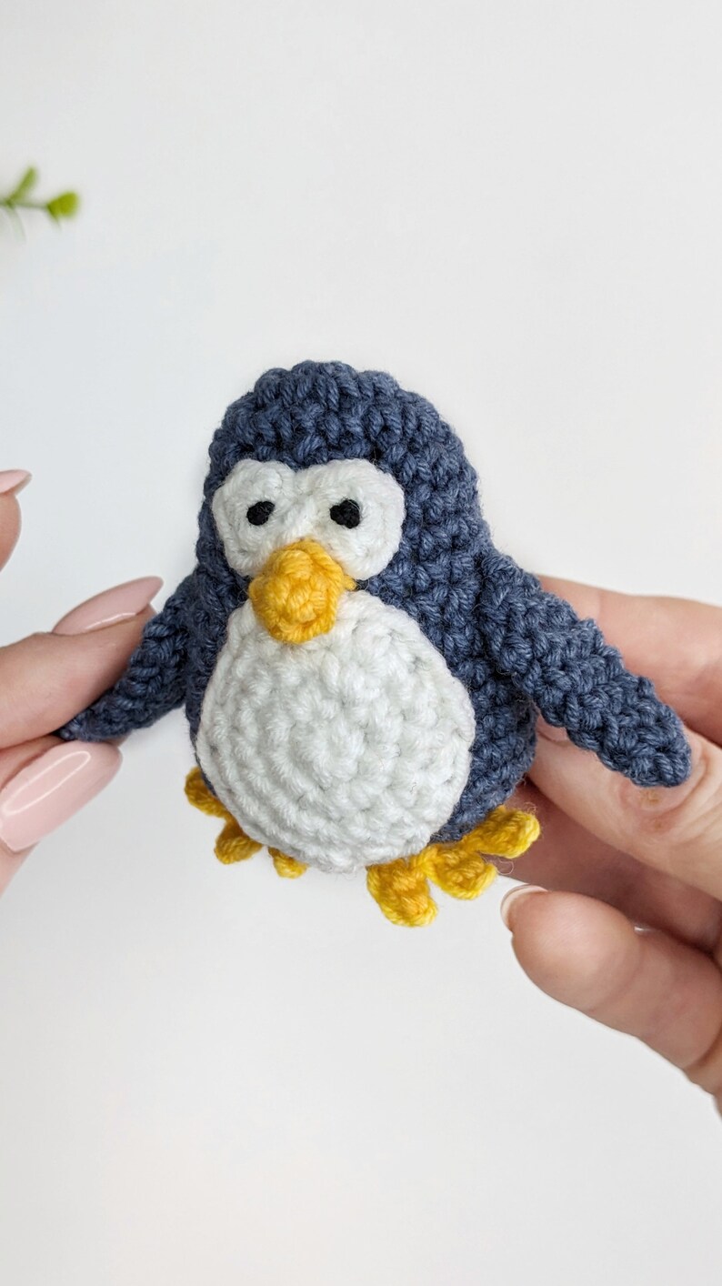 Pode incluir: Um pequeno brinquedo de pinguim de croch&ecirc; com corpo azul, barriga branca e bico e p&eacute;s amarelos.