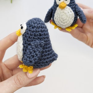 Pode incluir: Dois brinquedos de pinguim de croch&ecirc;. Um pinguim &eacute; azul com a barriga branca e p&eacute;s amarelos. O outro pinguim &eacute; branco com a barriga azul e p&eacute;s amarelos.
