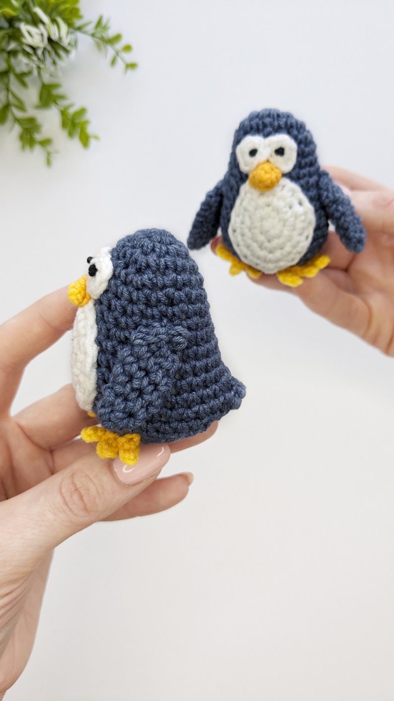 Pode incluir: Dois brinquedos de pinguim de croch&ecirc;. Um pinguim &eacute; azul com a barriga branca e p&eacute;s amarelos. O outro pinguim &eacute; branco com a barriga azul e p&eacute;s amarelos.