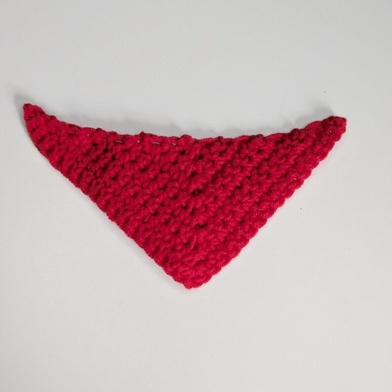 May include: A triangular bandana crafted from bright red yarn using a crochet technique. The accessory features a textured, open-stitch pattern throughout, forming a pointed shape with a wider top edge, showcasing consistent red fiber construction.