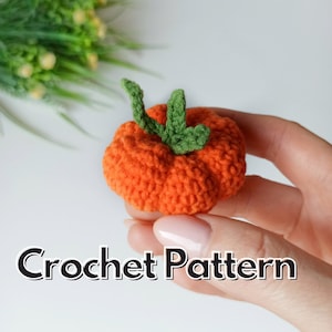 May include: A crocheted orange pumpkin with a green stem. The pumpkin is small and is being held in a hand. The text "Crochet Pattern" is visible below the pumpkin.