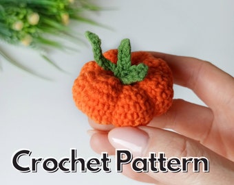 May include: A crocheted orange pumpkin with a green stem. The pumpkin is small and is being held in a hand. The text "Crochet Pattern" is visible below the pumpkin.