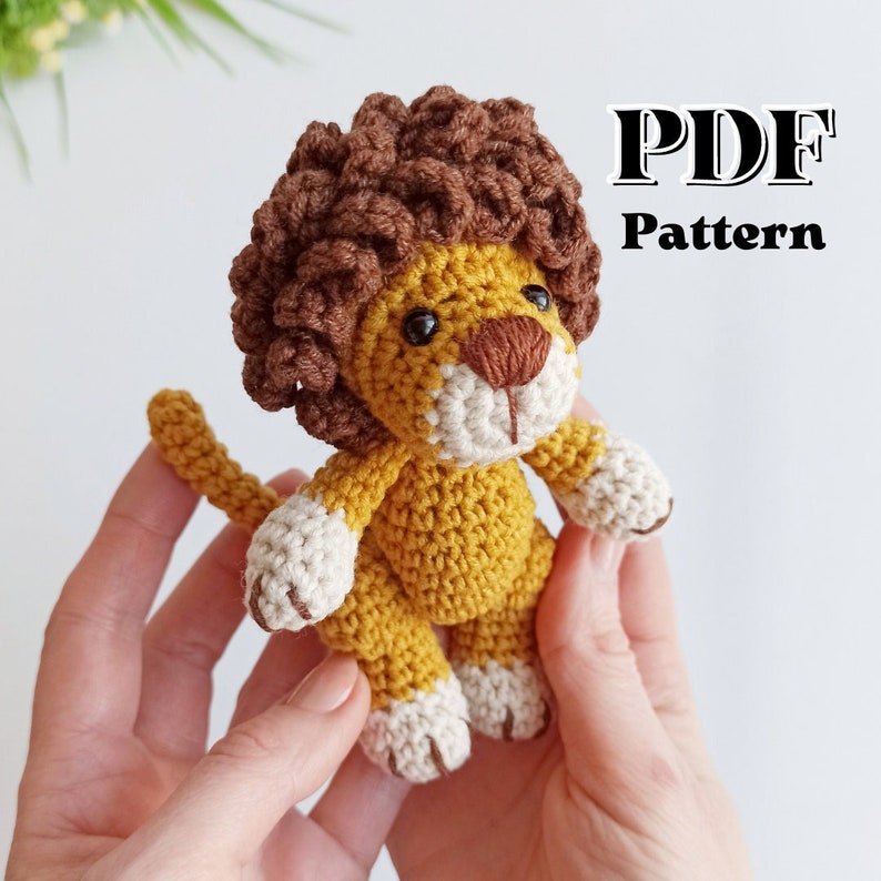 May include: Crochet pattern PDF for a cute lion amigurumi toy. The lion is brown and yellow with a fluffy mane and white paws.
