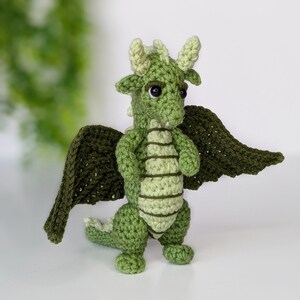 May include: Green crocheted dragon with wings, black eyes, and a light green stripe pattern on its body.