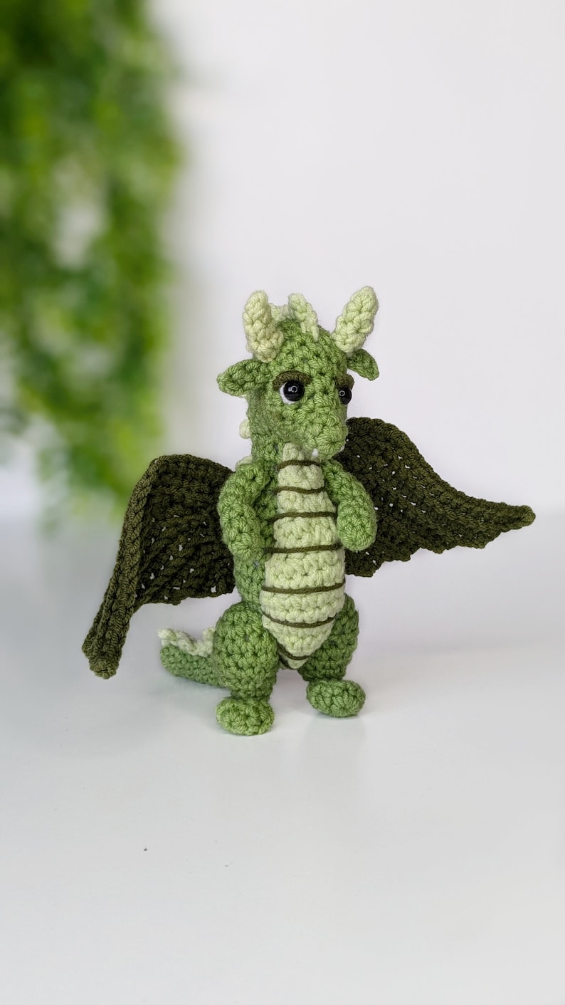 May include: Green crocheted dragon with wings, black eyes, and a light green stripe pattern on its body.