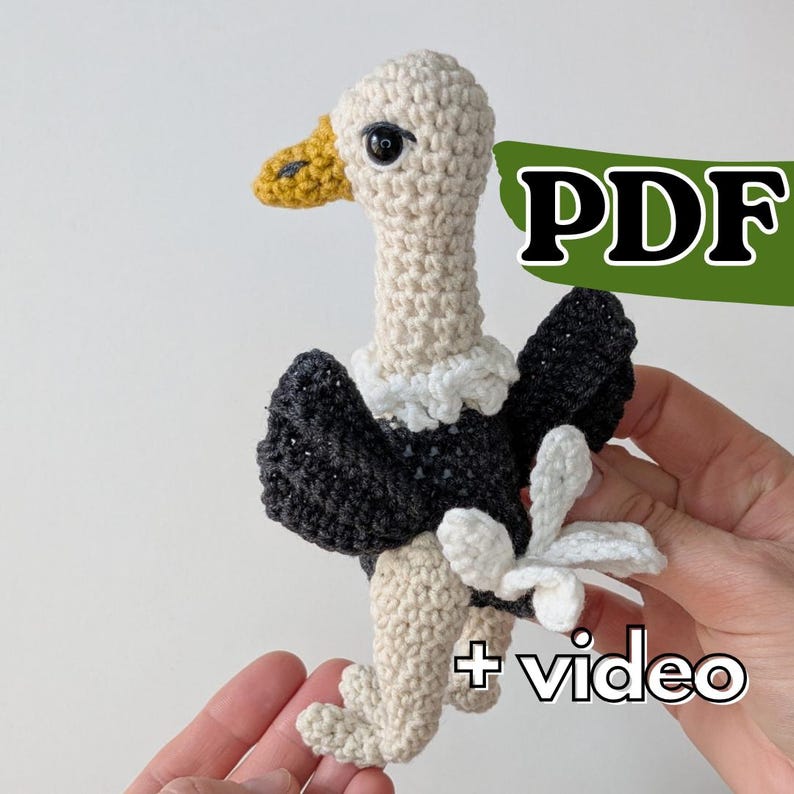 May include: A crocheted vulture toy with a cream-colored head and neck, a yellow beak, dark gray wings, and cream-colored legs. The toy features a white ruff around the neck and a white tail. The image includes the text PDF and + video.