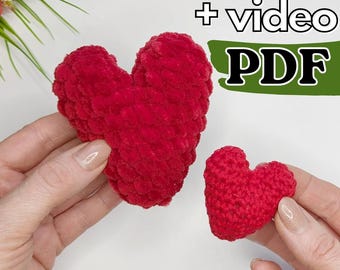 May include: Two handmade red crochet hearts, one large and one small, are held in hands. The hearts are made of a soft, textured yarn. The image includes the text "+ video PDF".