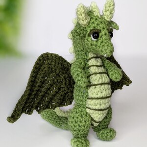 May include: A green crocheted dragon with large wings, black eyes, and a light green belly.