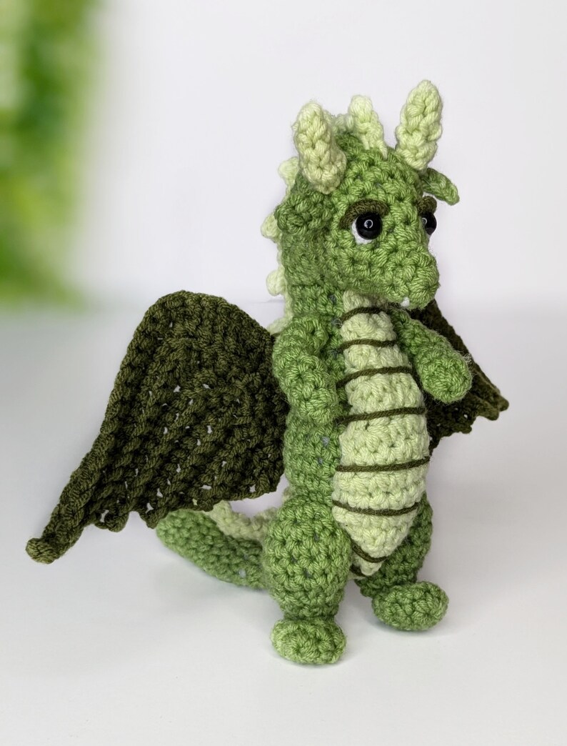 May include: A green crocheted dragon with large wings, black eyes, and a light green belly.