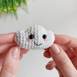 May include: A white crocheted cloud with black eyes and a pink smiling mouth.