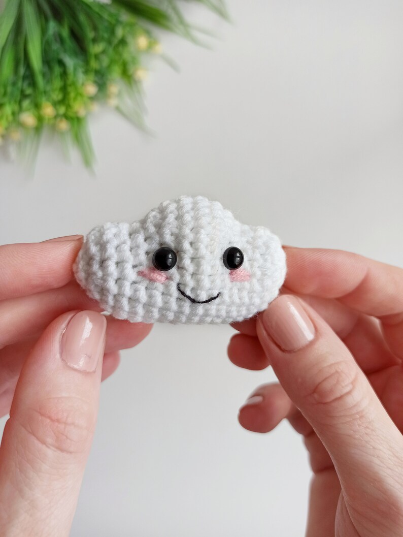 May include: A white crocheted cloud with black eyes and a pink smiling mouth.