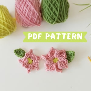 Puede incluir: Dos flores rosas de ganchillo con centros amarillos y hojas verdes. Las flores están sobre un fondo blanco. El texto "PDF PATTERN" está en letras verdes sobre un fondo blanco.