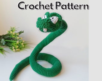 May include: A green crocheted snake with white eyes and teeth. The snake is curled up in a coil. Crochet Pattern.