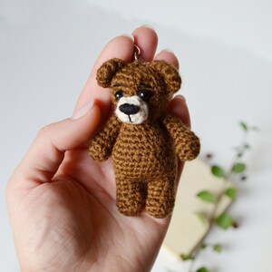 May include: A small brown crocheted teddy bear keychain with black eyes and a white nose.
