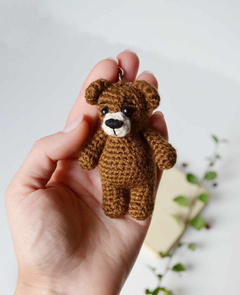 May include: A small brown crocheted teddy bear keychain with black eyes and a white nose.