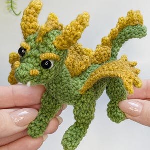 May include: A small crocheted dragon toy with green and yellow yarn. The dragon has a long tail, wings, and horns.