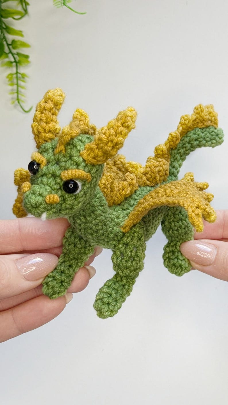 May include: A small crocheted dragon toy with green and yellow yarn. The dragon has a long tail, wings, and horns.