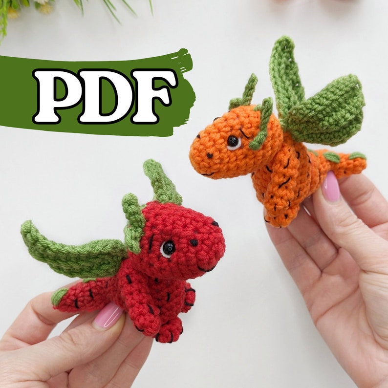 May include: Two crocheted dragon toys, one orange and one red, with green wings. The toys are made to look like fruit, with the orange dragon resembling a carrot and the red dragon resembling a strawberry.