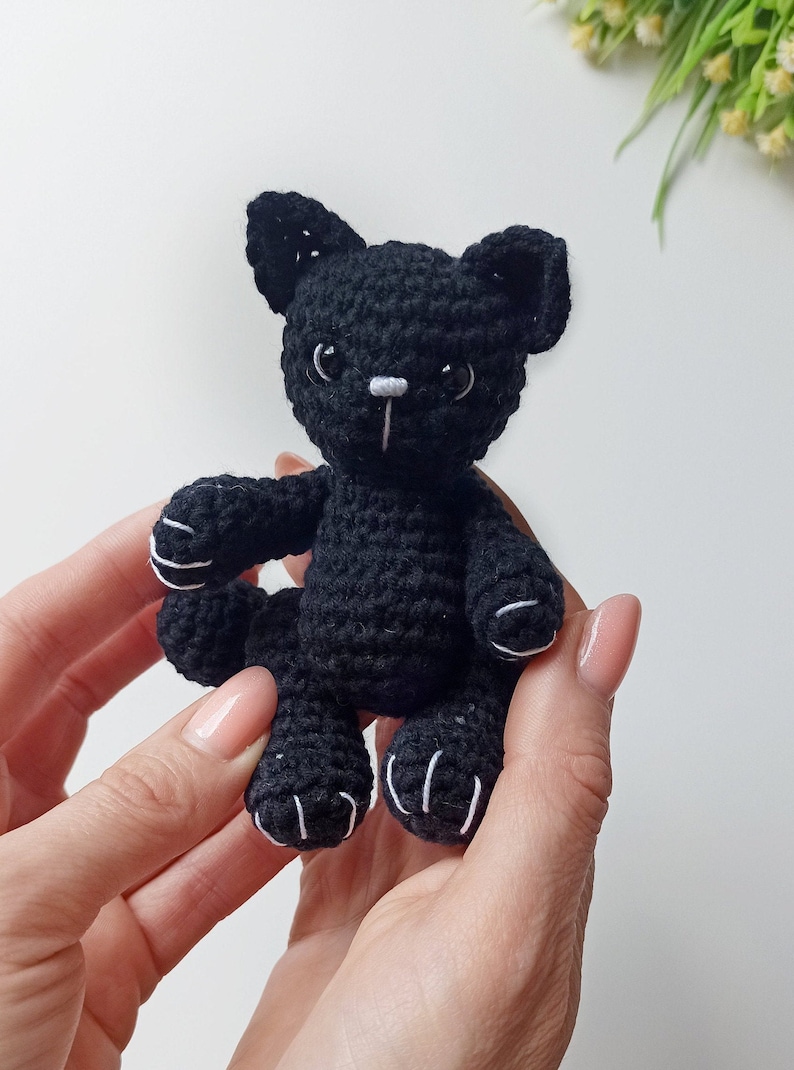 May include: A black crocheted cat toy with white accents on the eyes, nose, and paws.