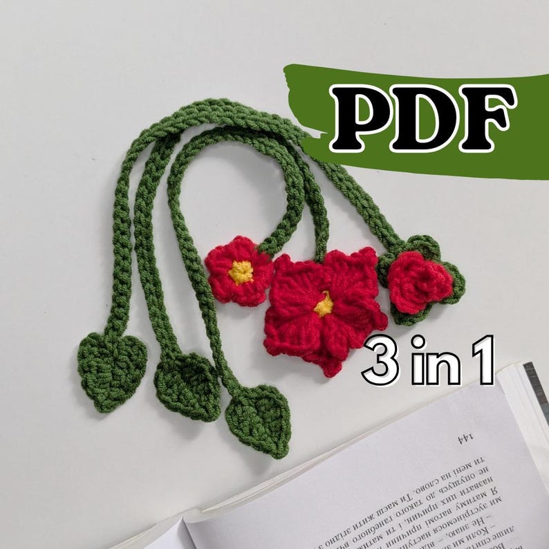 Puede incluir: Un marcap&aacute;ginas de ganchillo con tres flores rojas de centro amarillo y tallos verdes que terminan en hojas con forma de coraz&oacute;n. El texto PDF y 3 in 1 es visible en la imagen. El objeto est&aacute; colocado sobre un libro abierto de p&aacute;ginas blancas.
