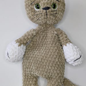 K&ouml;nnte beinhalten: Ein handgefertigtes Pl&uuml;schkatzenspielzeug in Beige- und Wei&szlig;t&ouml;nen. Die Katze hat einen strukturierten, pl&uuml;schigen K&ouml;rper mit wei&szlig;en Pfoten, Ohren und Schwanzspitze. Es hat gr&uuml;ne Augen, schwarze Schnurrhaare und eine gen&auml;hte Nase und Mund.