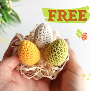 May include: Three crocheted Easter eggs in a nest of shredded paper. The eggs are yellow, green, and white.