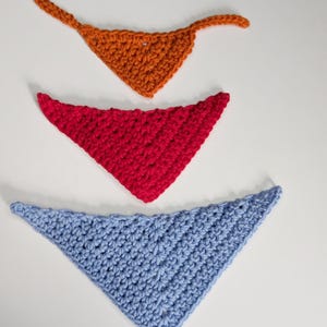 May include: Three triangular crochet bandanas arranged vertically. The top bandana is orange with two thin ties, the middle bandana is bright red, and the bottom bandana is light blue. Each piece features a textured, hand-stitched yarn pattern.