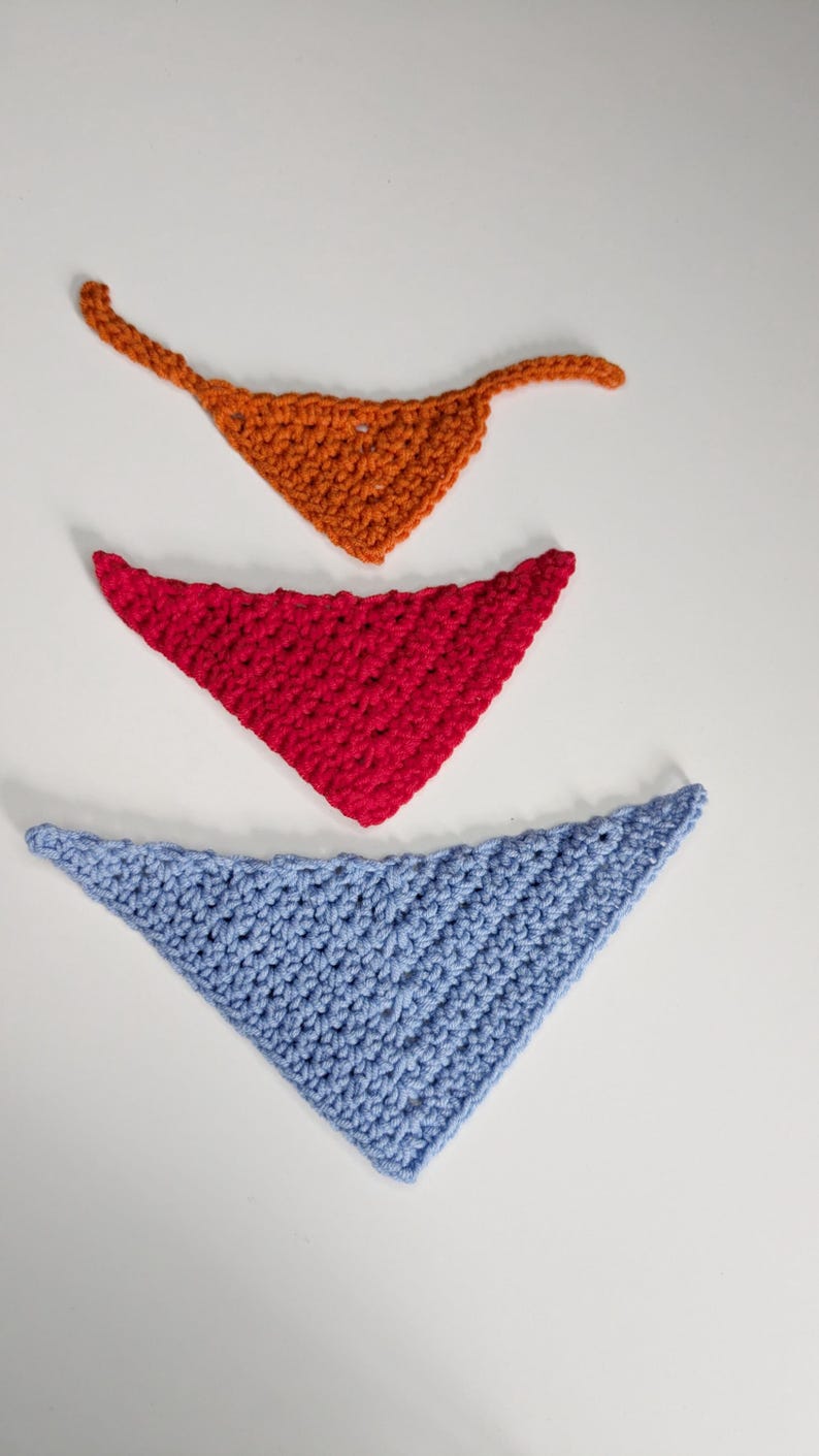 May include: Three triangular crochet bandanas arranged vertically. The top bandana is orange with two thin ties, the middle bandana is bright red, and the bottom bandana is light blue. Each piece features a textured, hand-stitched yarn pattern.