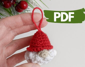 May include: A crocheted gnome ornament with a red hat and white beard. The gnome has a small brown nose and is holding a loop of red yarn for hanging.
