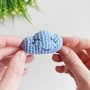 May include: A light blue crocheted cloud with a smiling face. The cloud is being held in two hands.